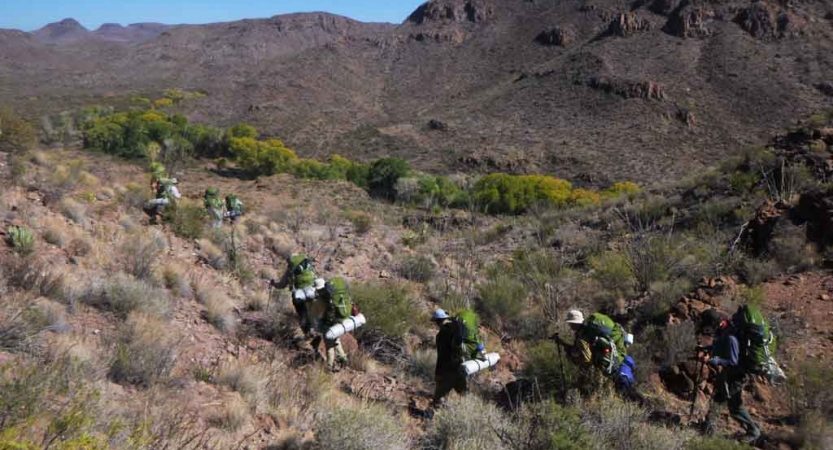 a group of gap year students wearing backpacks hike through a desert landscape on an outward bound semester expedition 